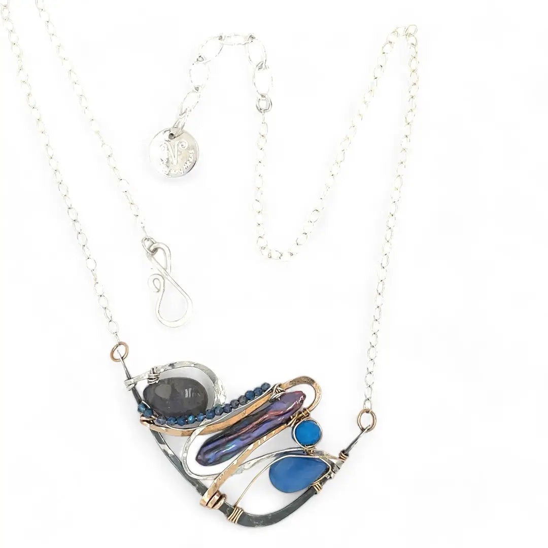 Darkened sterling silver boomerang shaped pendant necklace with waves of hammered bronze, sterling silver, and gold filled wire holding smooth labradorite, blue jade, blue crystal, and a purple fresh water stick pearl in place