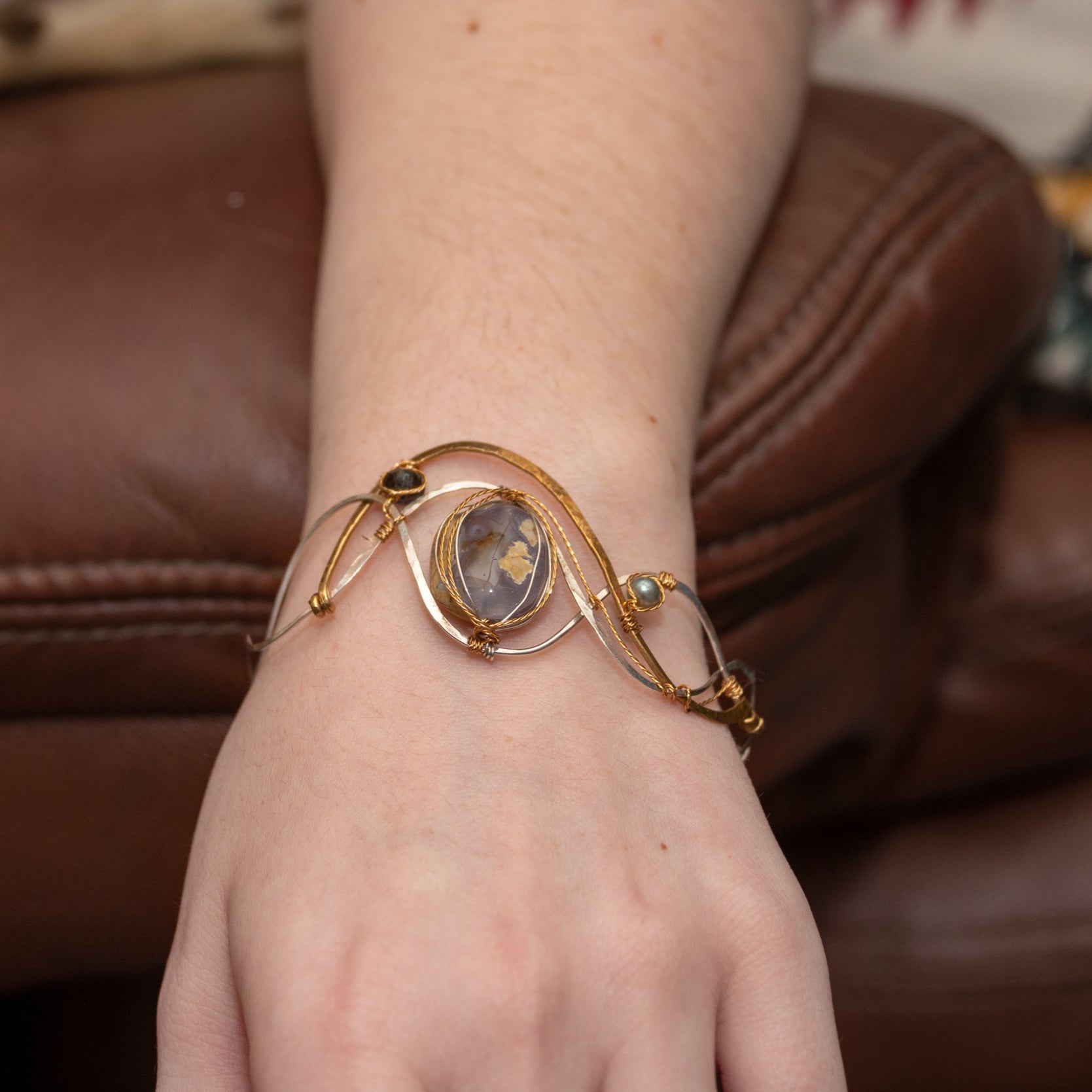 light purple chalcedony smooth nugget surrounded by layers of hammered sterling silver and brass wires to form a statement bracelet accented with fresh water pearl and crystal