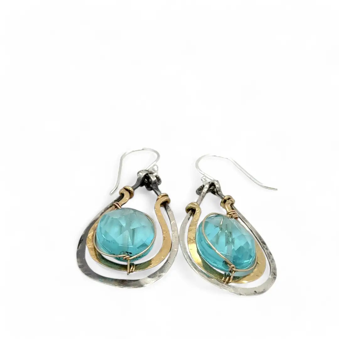 A pair of handcrafted oxidized sterling silver drop earrings with hammered brass, aqua blue quartz crystal centers and gold-filled details