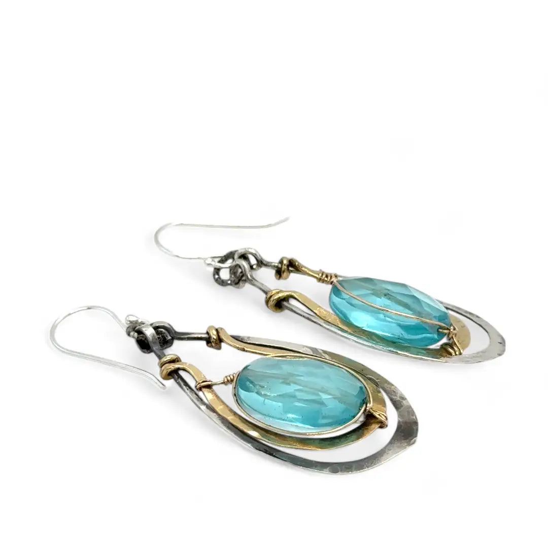 A pair of handcrafted oxidized sterling silver drop earrings with hammered brass, aqua blue quartz crystal centers and gold-filled details
