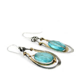 A pair of handcrafted oxidized sterling silver drop earrings with hammered brass, aqua blue quartz crystal centers and gold-filled details