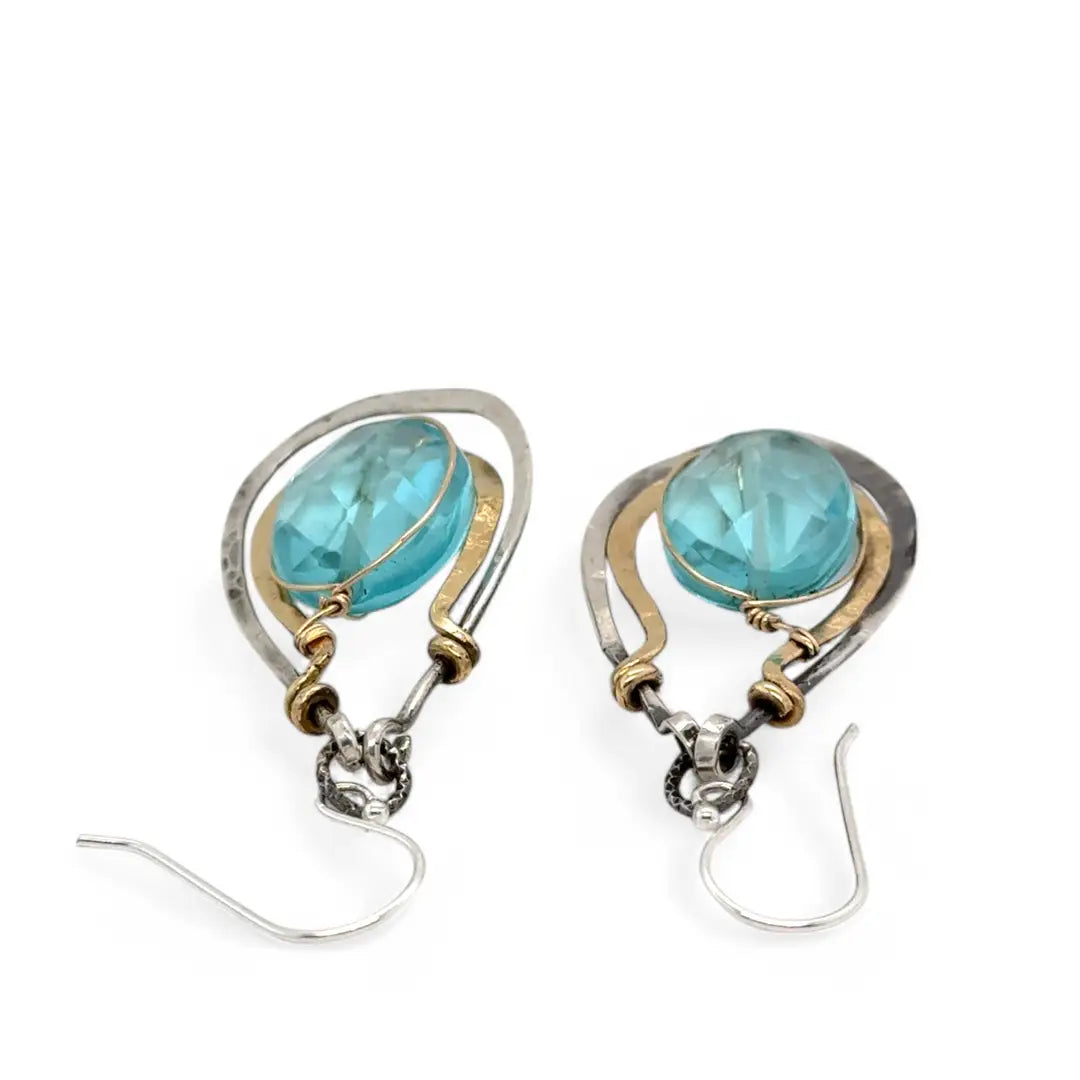 A pair of handcrafted oxidized sterling silver drop earrings with hammered brass, aqua blue quartz crystal centers and gold-filled details
