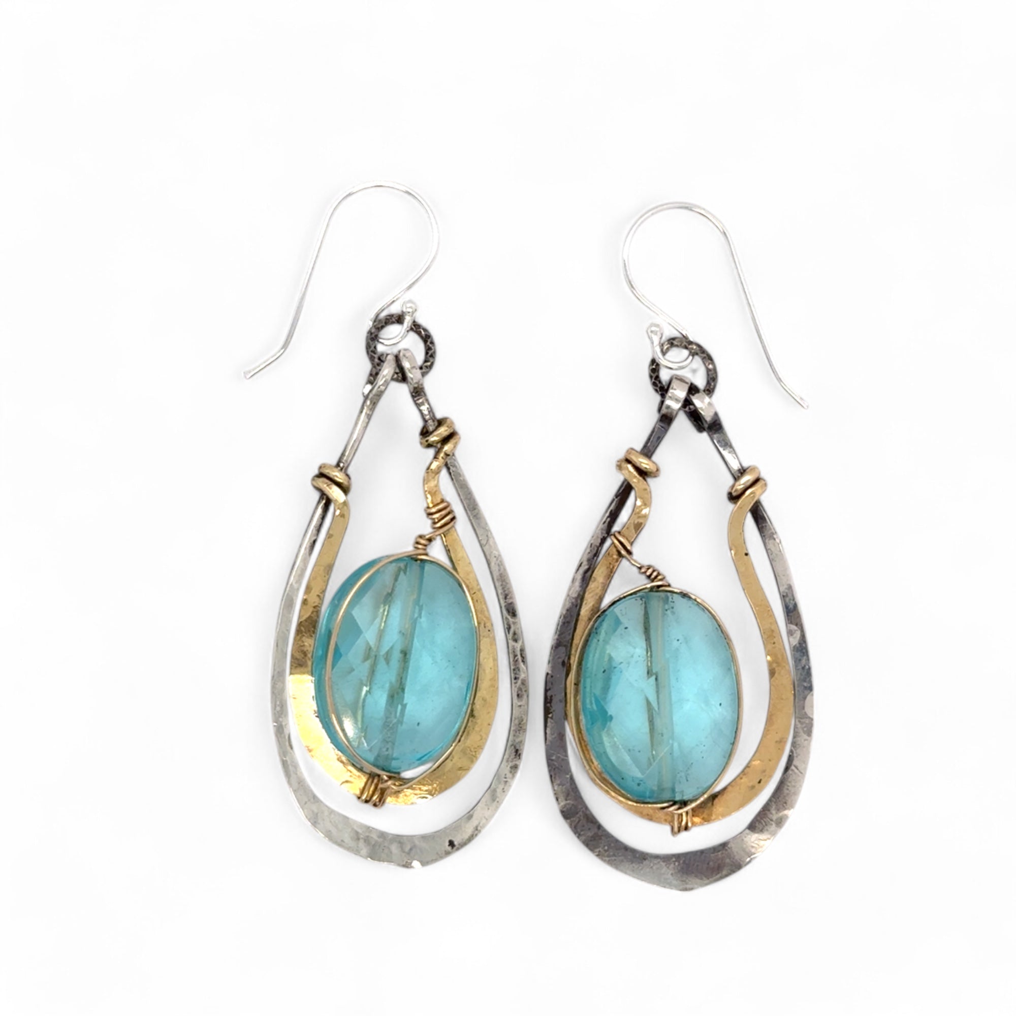 A pair of handcrafted oxidized sterling silver drop earrings with hammered brass, aqua blue quartz crystal centers and gold-filled details