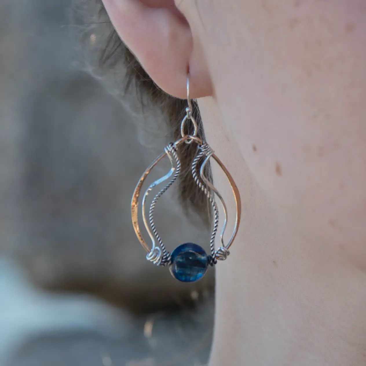 A bronze hoop earring with sparkly sterling silver and oxidized twisted sterling silver swishes holding a blue kyanite stone.