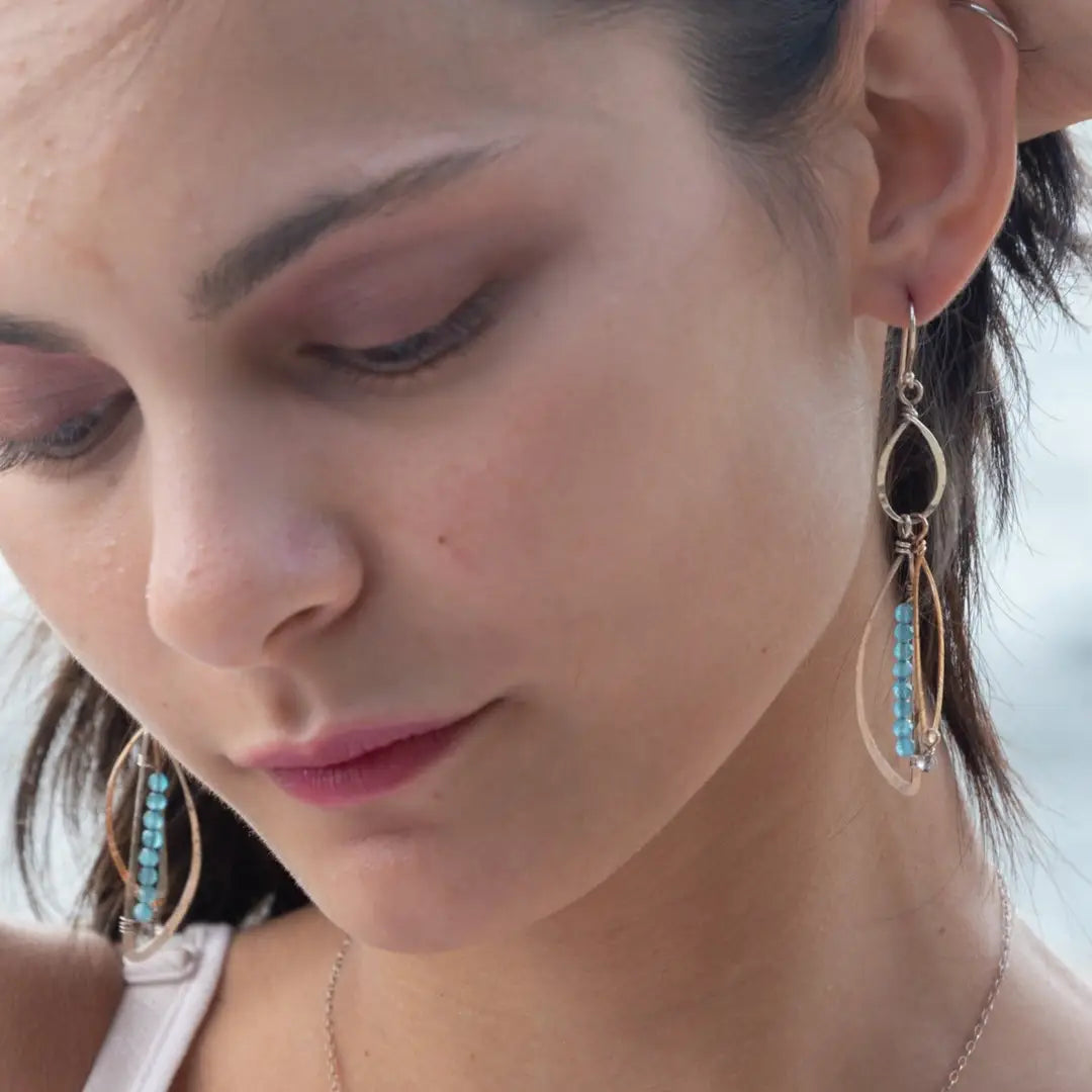 A pair of dangling earrings with sterling silver and bronze semi-circle elements, accented with tiny faceted aqua cat's eye gemstones and labradorite dangles