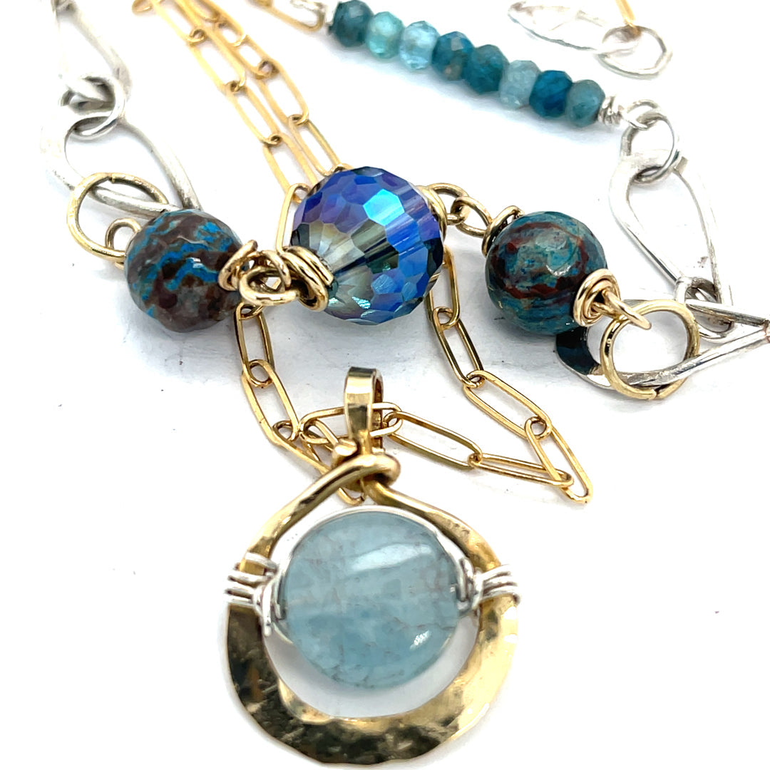 A sterling silver handmade chain link necklace with a brass charm holding an aquamarine coin, with faceted chrysocolla, apatite and blue disco ball crystal on gold filled delicate chain