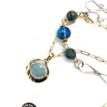 A sterling silver handmade chain link necklace with a brass charm holding an aquamarine coin, with faceted chrysocolla, apatite and blue disco ball crystal on gold filled delicate chain