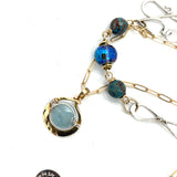 A sterling silver handmade chain link necklace with a brass charm holding an aquamarine coin, with faceted chrysocolla, apatite and blue disco ball crystal on gold filled delicate chain