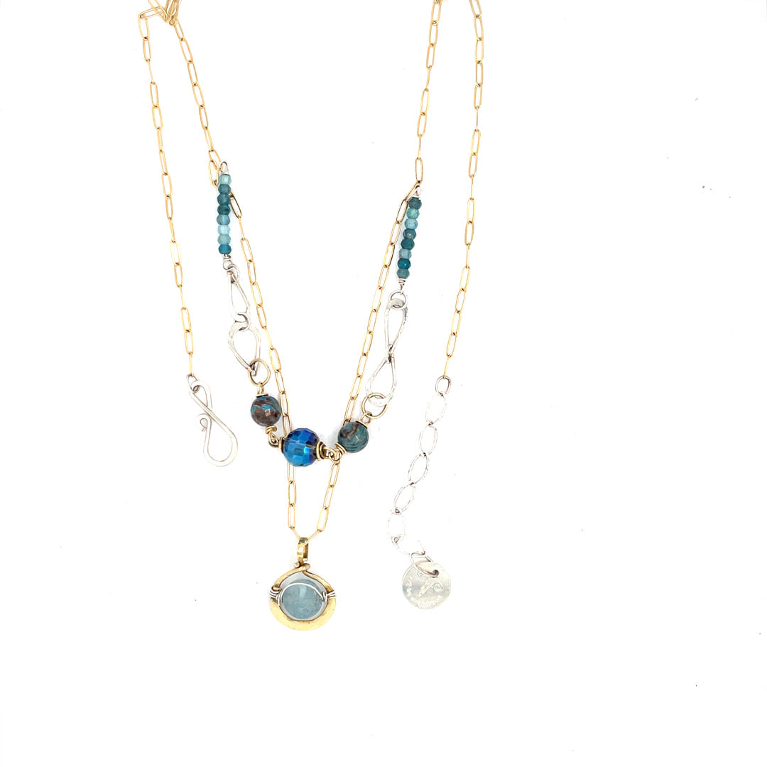 A sterling silver handmade chain link necklace with a brass charm holding an aquamarine coin, with faceted chrysocolla, apatite and blue disco ball crystal on gold filled delicate chain