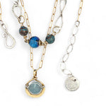A sterling silver handmade chain link necklace with a brass charm holding an aquamarine coin, with faceted chrysocolla, apatite and blue disco ball crystal on gold filled delicate chain