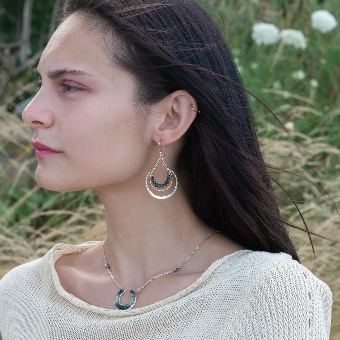 Blue tourmaline gemstones line the inside of a brass ring with hammered sterling silver outside ring, hanging from a sterling silver bar chain