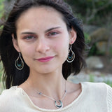 Blue tourmaline gemstones line the inside of a brass ring with hammered sterling silver outside ring, hanging from a sterling silver bar chain