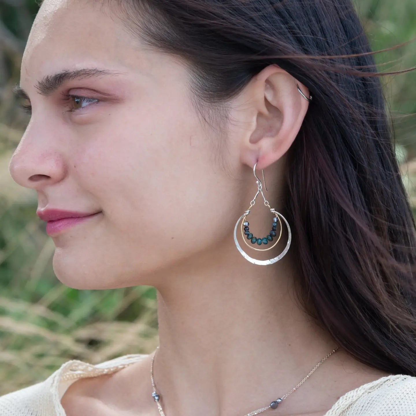Blue tourmaline gemstones line the inside of a brass ring with hammered sterling silver outside ring, hanging from a sterling silver bar chain