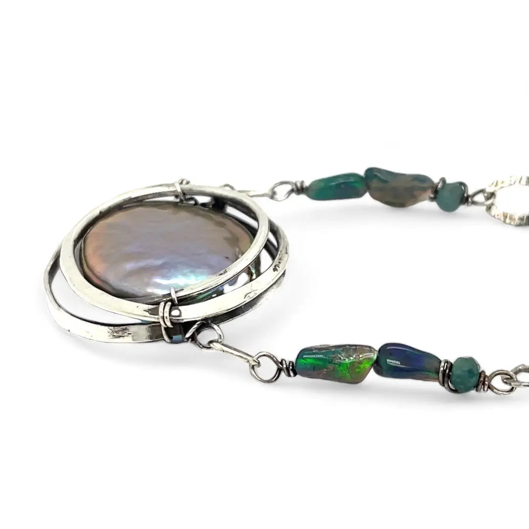 A sterling silver chain link necklace with a blue purple fresh water pearl coin in a hammered silver knot pendant, accented with blue opal and blue tourmaline gemstones