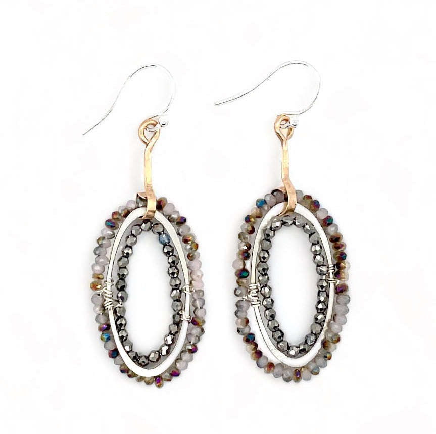 A pair of drop earrings featuring micro faceted blush crystals in two rows around a hammered silver ring, with bronze stems and French hooks.