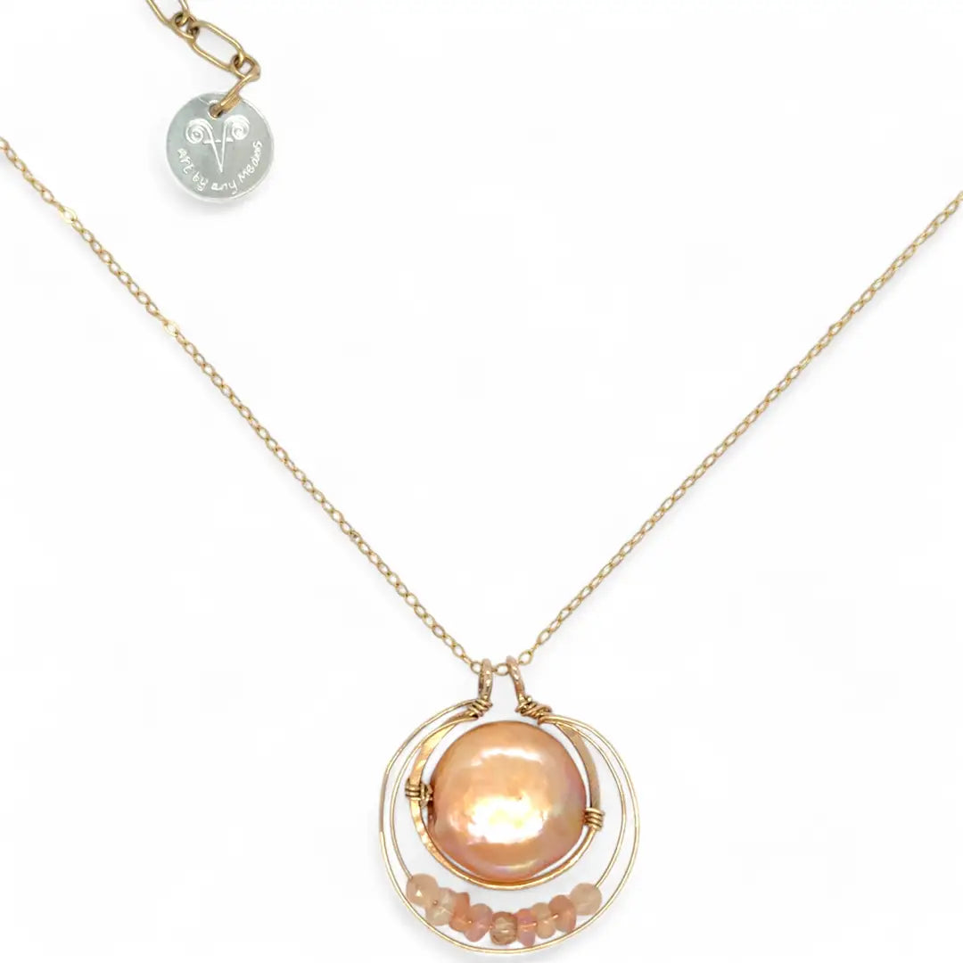 A gold-filled chain necklace with a pearl pink pearl coin inside a bronze ring wrapped in gold-filled rings with a layer of peach cat's eye and pink opal gemstones