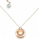 A gold-filled chain necklace with a pearl pink pearl coin inside a bronze ring wrapped in gold-filled rings with a layer of peach cat's eye and pink opal gemstones