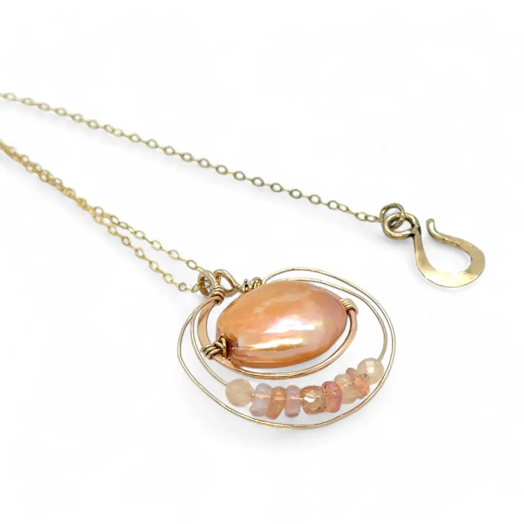 A gold-filled chain necklace with a pearl pink pearl coin inside a bronze ring wrapped in gold-filled rings with a layer of peach cat's eye and pink opal gemstones