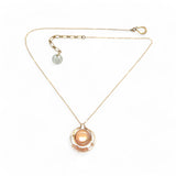 A gold-filled chain necklace with a pearl pink pearl coin inside a bronze ring wrapped in gold-filled rings with a layer of peach cat's eye and pink opal gemstones