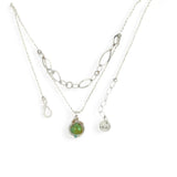 A silver-colored necklace with a teardrop-shaped pendant featuring a bright green turquoise gemstone, accented with a small chalcedony gemstone , and a handmade sterling silver link chain.
