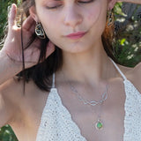 A silver-colored necklace with a teardrop-shaped pendant featuring a bright green turquoise gemstone, accented with a small chalcedony gemstone , and a handmade sterling silver link chain.