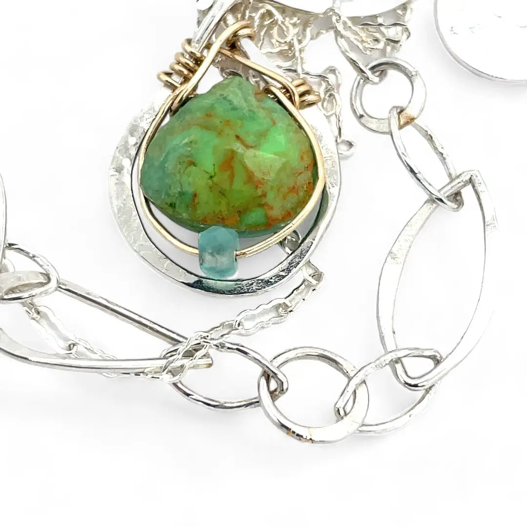 A silver-colored necklace with a teardrop-shaped pendant featuring a bright green turquoise gemstone, accented with a small chalcedony gemstone , and a handmade sterling silver link chain.