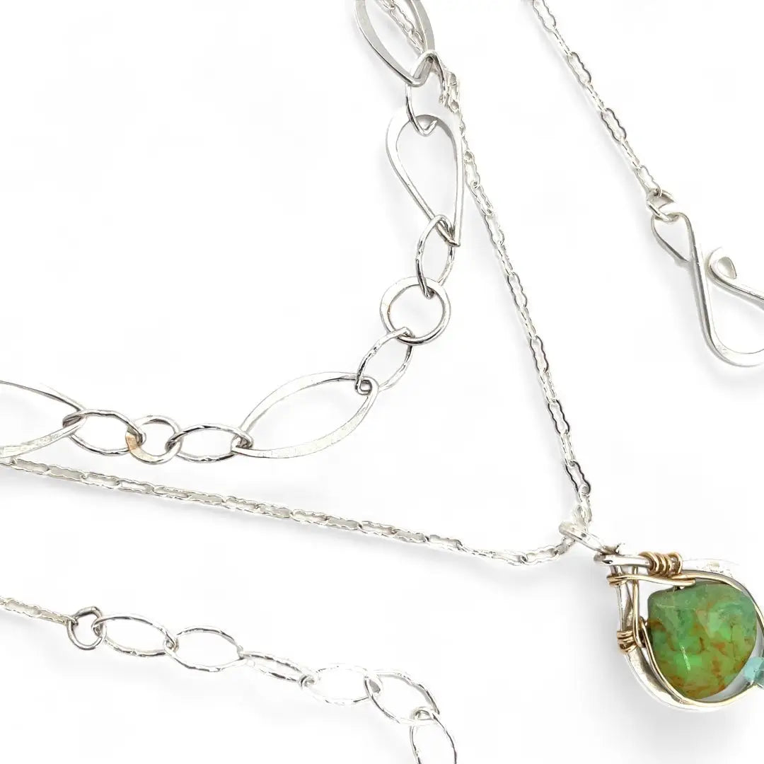 A silver-colored necklace with a teardrop-shaped pendant featuring a bright green turquoise gemstone, accented with a small chalcedony gemstone , and a handmade sterling silver link chain.