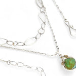 A silver-colored necklace with a teardrop-shaped pendant featuring a bright green turquoise gemstone, accented with a small chalcedony gemstone , and a handmade sterling silver link chain.