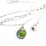 A silver-colored necklace with a teardrop-shaped pendant featuring a bright green turquoise gemstone, accented with a small chalcedony gemstone , and a handmade sterling silver link chain.