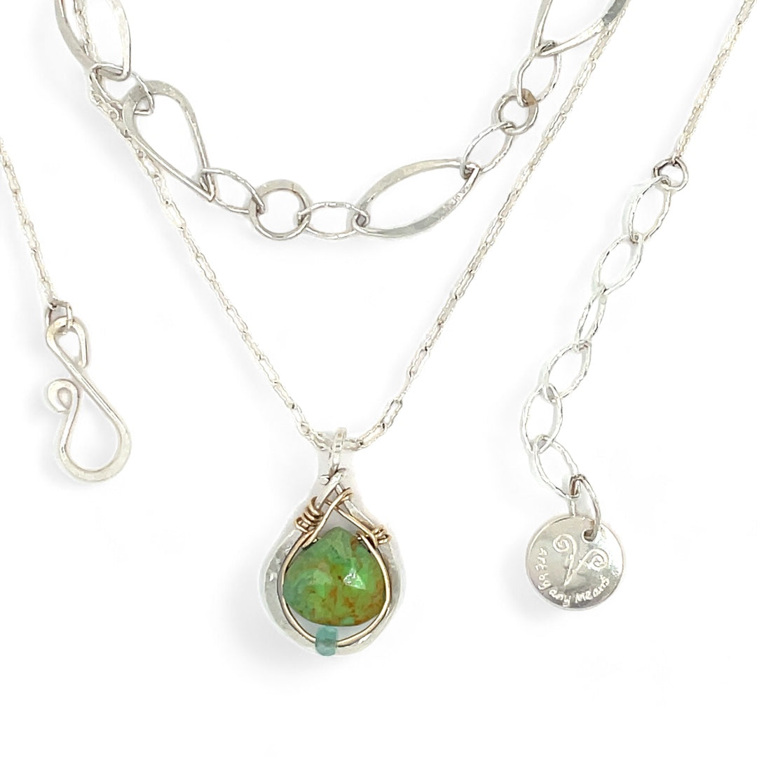A silver-colored necklace with a teardrop-shaped pendant featuring a bright green turquoise gemstone, accented with a small chalcedony gemstone , and a handmade sterling silver link chain.
