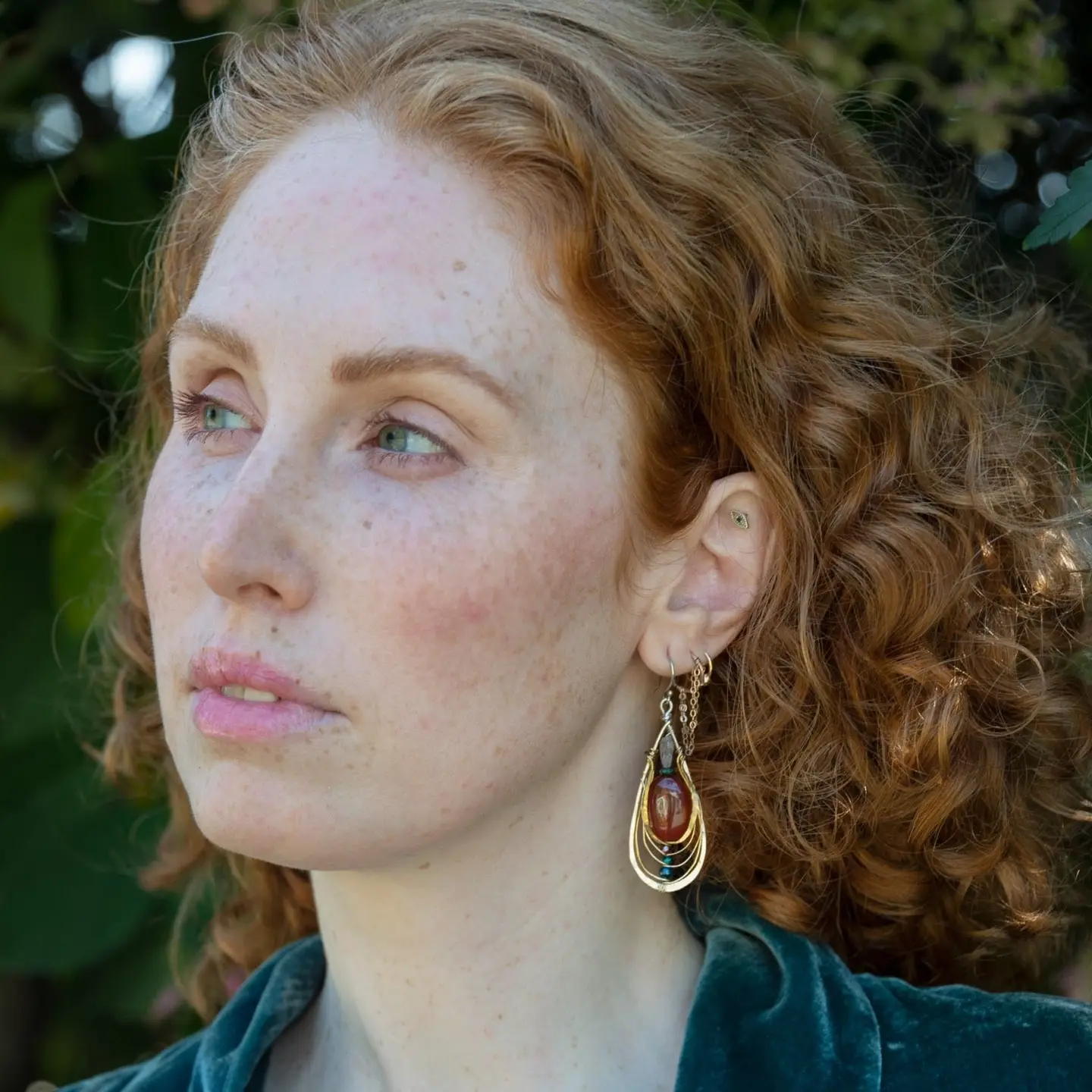 Sterling silver handmade drop earrings with carnelian, pyrite, blue fresh water pearl, red cubic zirconia, and green amethyst carved hand within layers of gold filled and brass wires