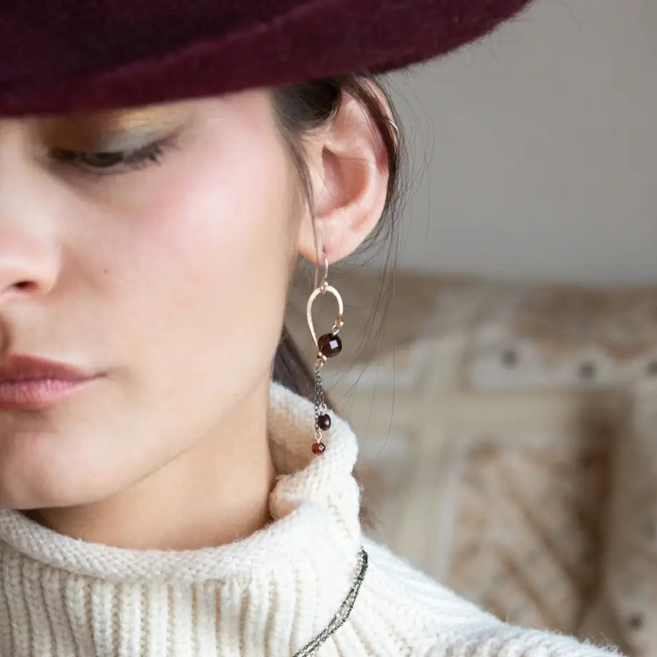A pair of cascade style garnet earrings with faceted sphere gemstones, handmade brass hoops, and suspending oxidized sterling silver chains with a deep red freshwater pearl.