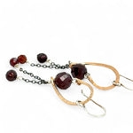 A pair of cascade style garnet earrings with faceted sphere gemstones, handmade brass hoops, and suspending oxidized sterling silver chains with a deep red freshwater pearl.