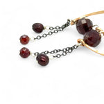 A pair of cascade style garnet earrings with faceted sphere gemstones, handmade brass hoops, and suspending oxidized sterling silver chains with a deep red freshwater pearl.