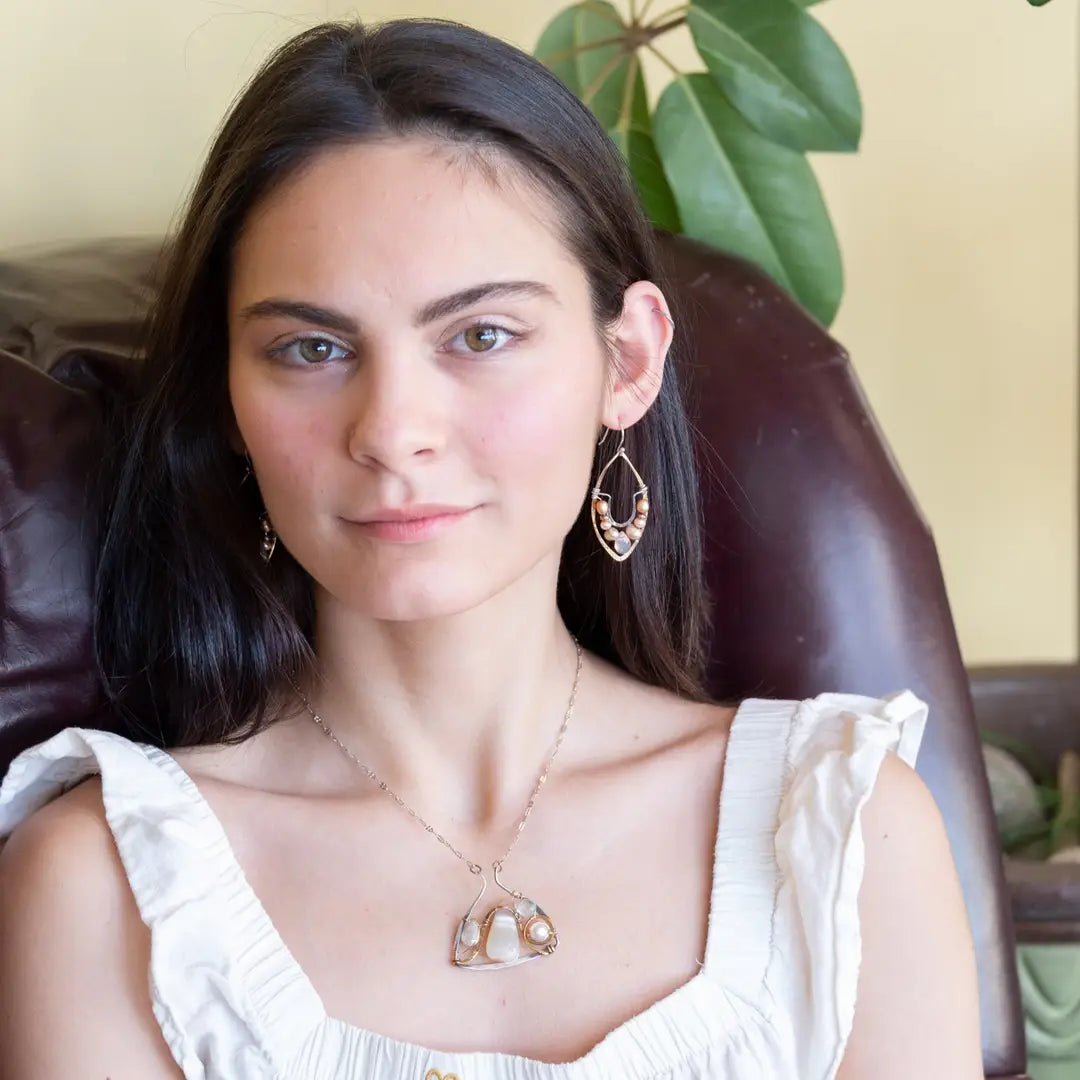 Pink and champagne colored fresh water pearls combined with a peach opalescent faceted drop gemstone sit inside a brass stamped marquise earring with sterling silver accent