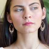 Pink and champagne colored fresh water pearls combined with a peach opalescent faceted drop gemstone sit inside a brass stamped marquise earring with sterling silver accent