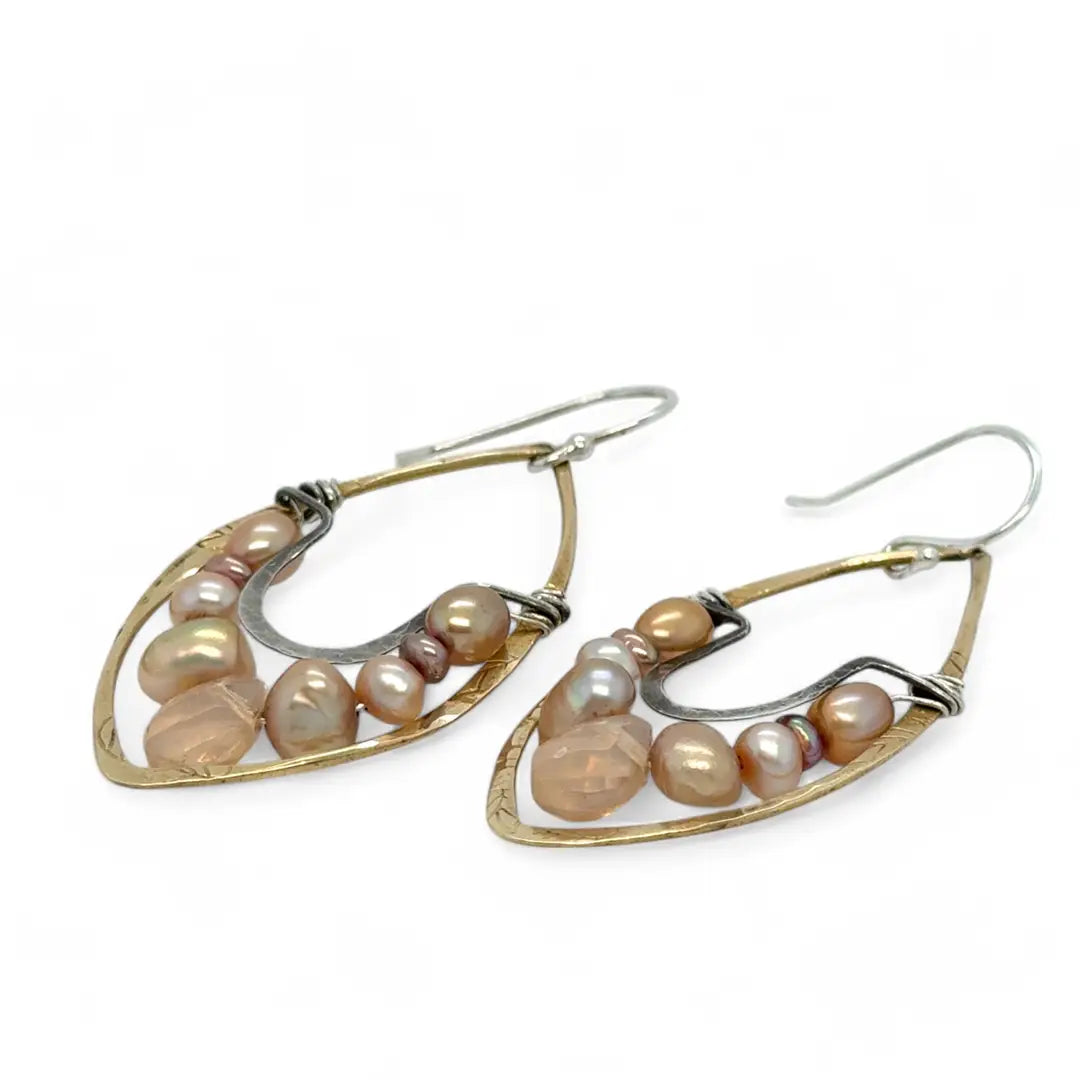 Pink and champagne colored fresh water pearls combined with a peach opalescent faceted drop gemstone sit inside a brass stamped marquise earring with sterling silver accent