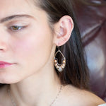 Pink and champagne colored fresh water pearls combined with a peach opalescent faceted drop gemstone sit inside a brass stamped marquise earring with sterling silver accent