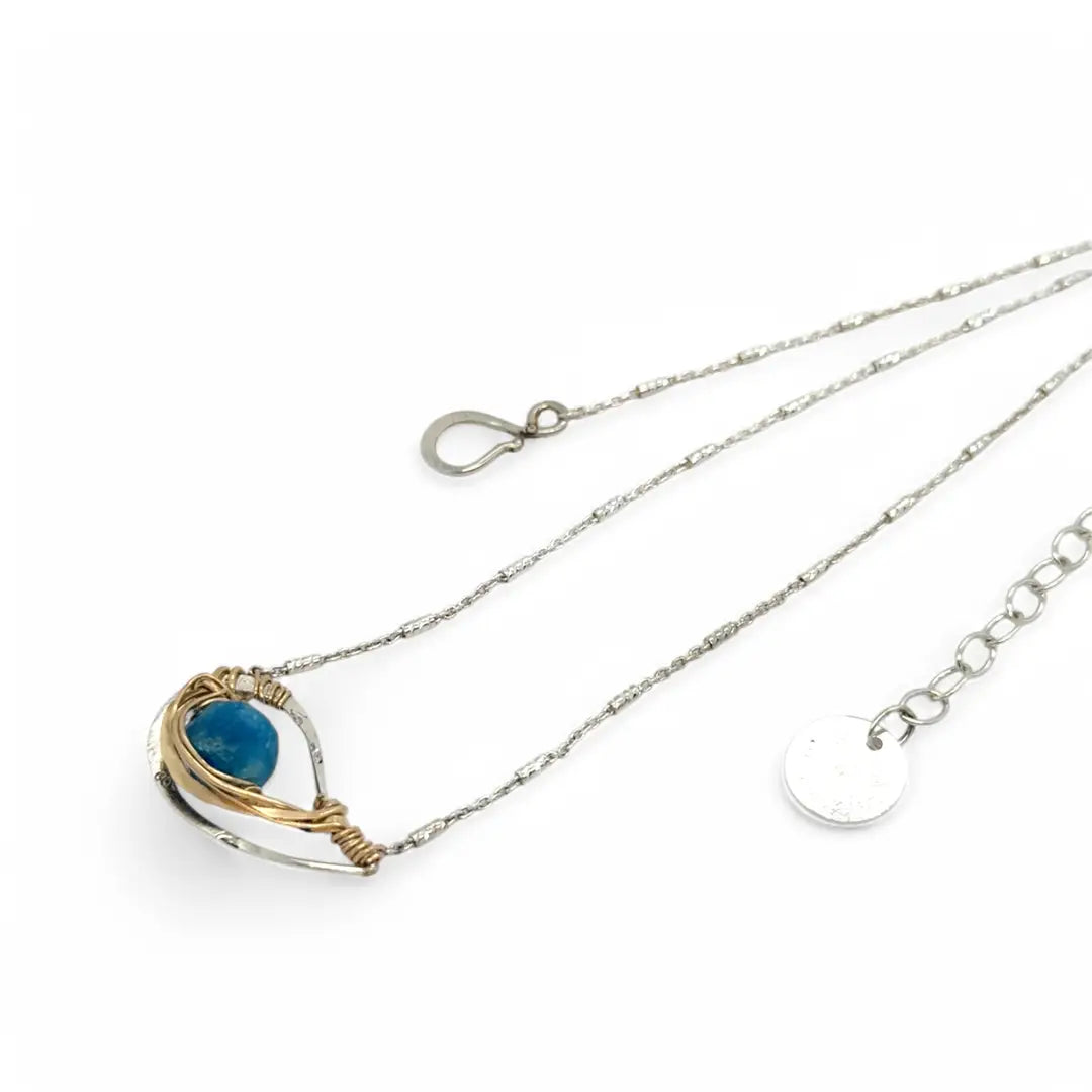 a singular faceted apatite gemstone is held in layered of hammered gold filled wire on a mini sterling silver paisley necklace