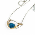a singular faceted apatite gemstone is held in layered of hammered gold filled wire on a mini sterling silver paisley necklace