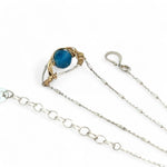 a singular faceted apatite gemstone is held in layered of hammered gold filled wire on a mini sterling silver paisley necklace