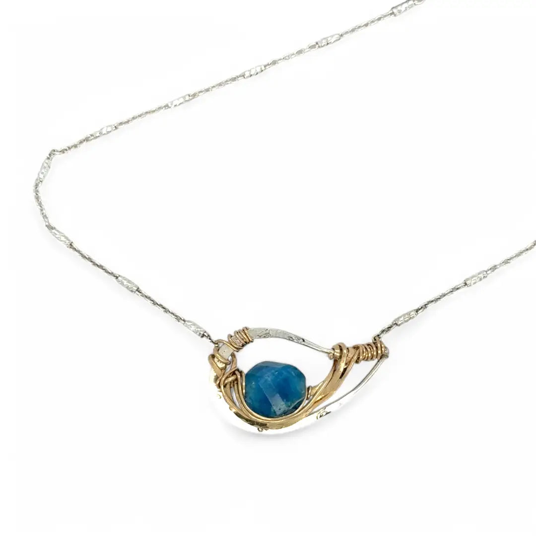 a singular faceted apatite gemstone is held in layered of hammered gold filled wire on a mini sterling silver paisley necklace