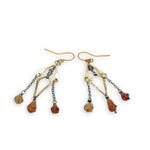 fire shaped carved hessonite garnet gemstones dangle from dark sterling silver delicate chain and brass arches and diamond earrings