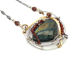A necklace with teardrop-shaped labradorite gemstone adorned with faceted hessonite gemstones and set between hammered arcs of brass and oxidized sterling twist inside a sterling silver semi circle pendant. 