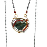 A necklace with teardrop-shaped labradorite gemstone adorned with faceted hessonite gemstones and set between hammered arcs of brass and oxidized sterling twist inside a sterling silver semi circle pendant. 