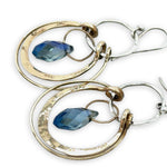 Blue crystal drop held within circles of brass stamped rings handing on a sterling silver hoop