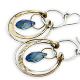 Blue crystal drop held within circles of brass stamped rings handing on a sterling silver hoop