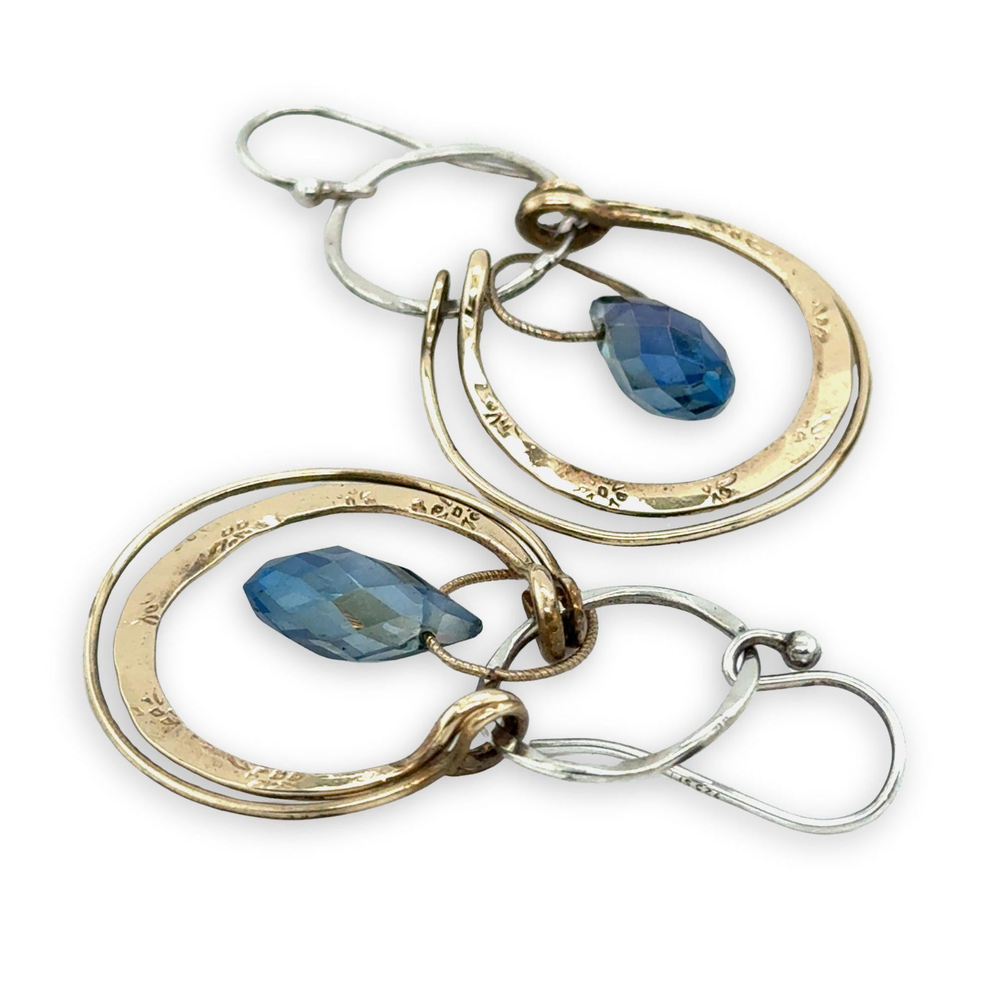 Blue crystal drop held within circles of brass stamped rings handing on a sterling silver hoop