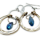 Blue crystal drop held within circles of brass stamped rings handing on a sterling silver hoop