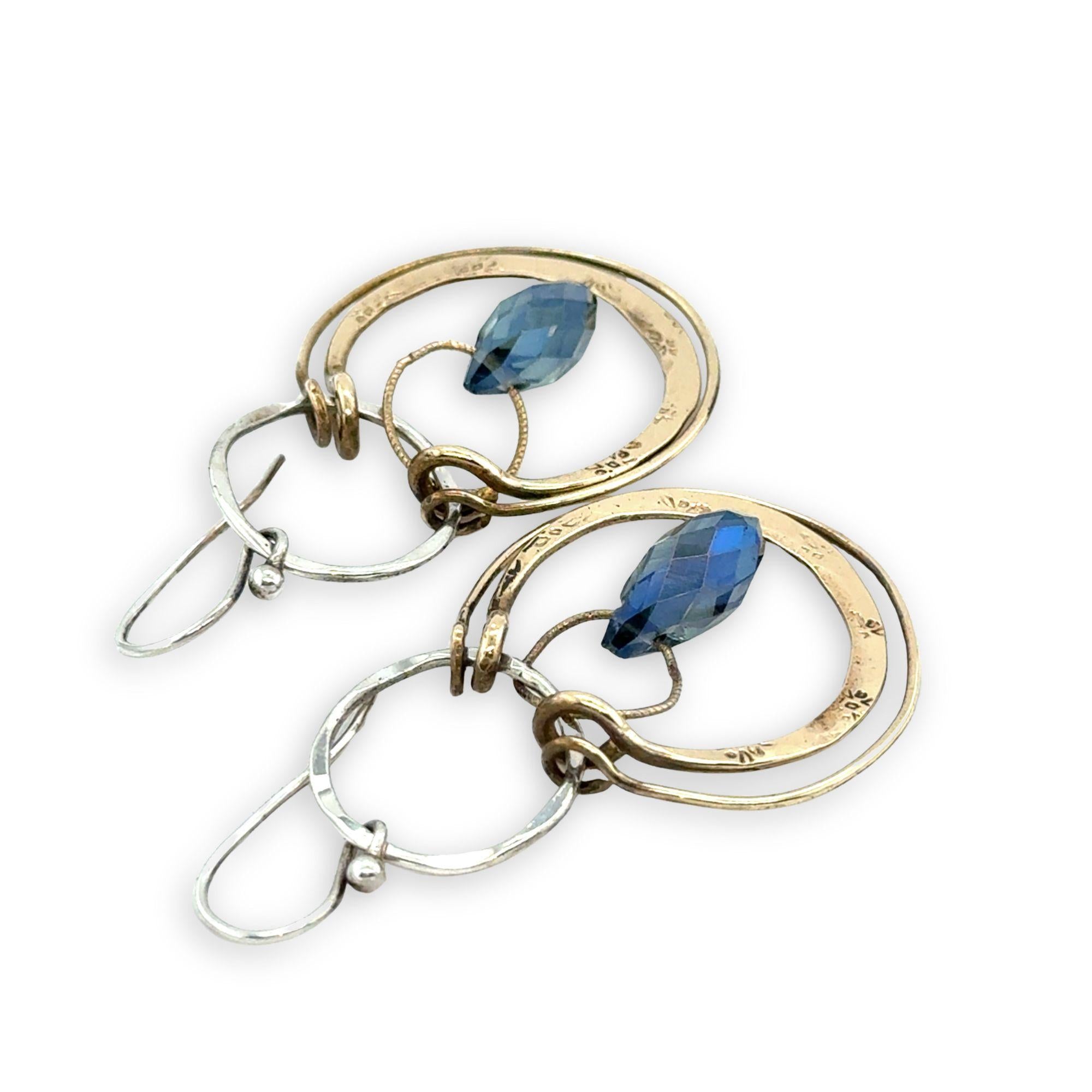 Blue crystal drop held within circles of brass stamped rings handing on a sterling silver hoop